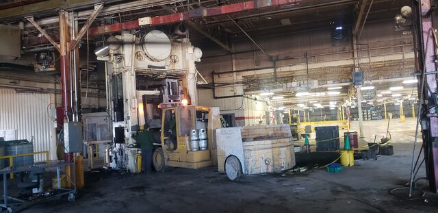 A straight-side press still standing on the plant floor, forklift working in at its base