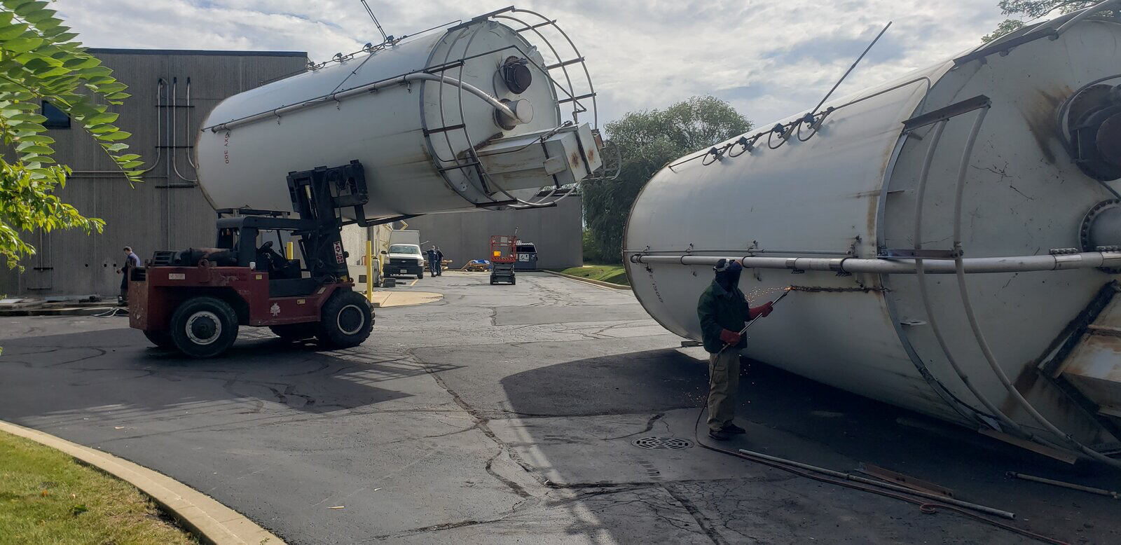A red forklift handling a large white tank outdoors, with a second tank lying in the foreground