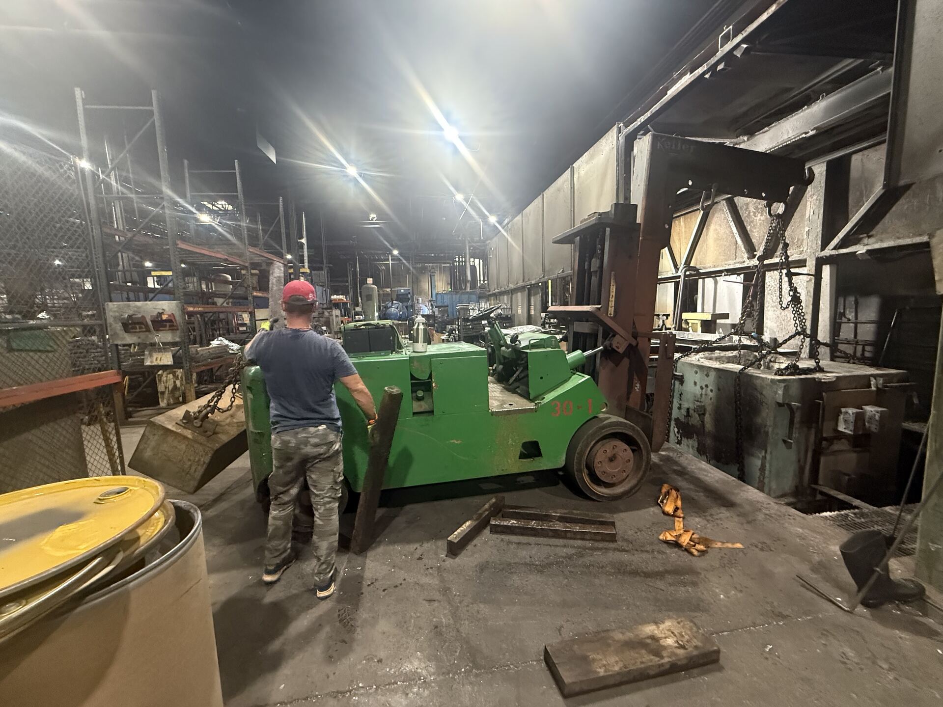 A man guiding a green forklift with a machine in a dim old plant