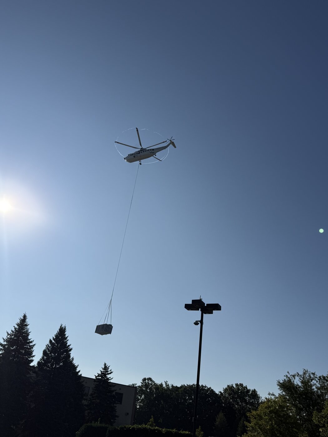 A rooftop condensing unit hanging on a long line well below the helicopter, showing how much rope separates the aircraft from the load