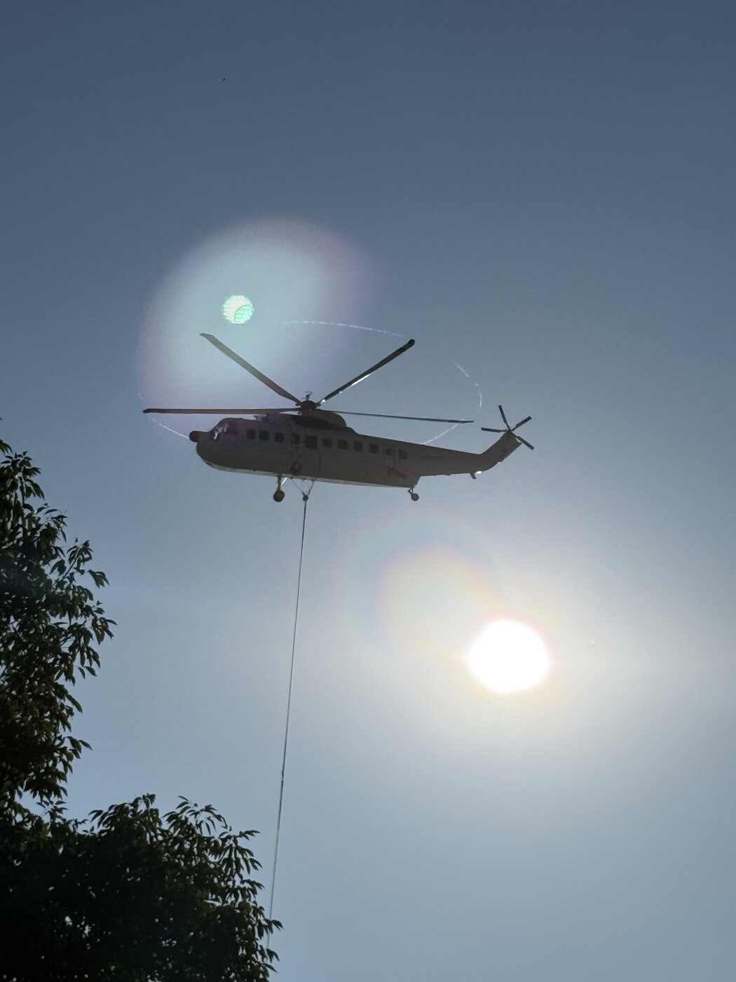The heavy lift Sikorsky hovering directly overhead with its line running down out of frame, on a rooftop unit change-out west of Chicago