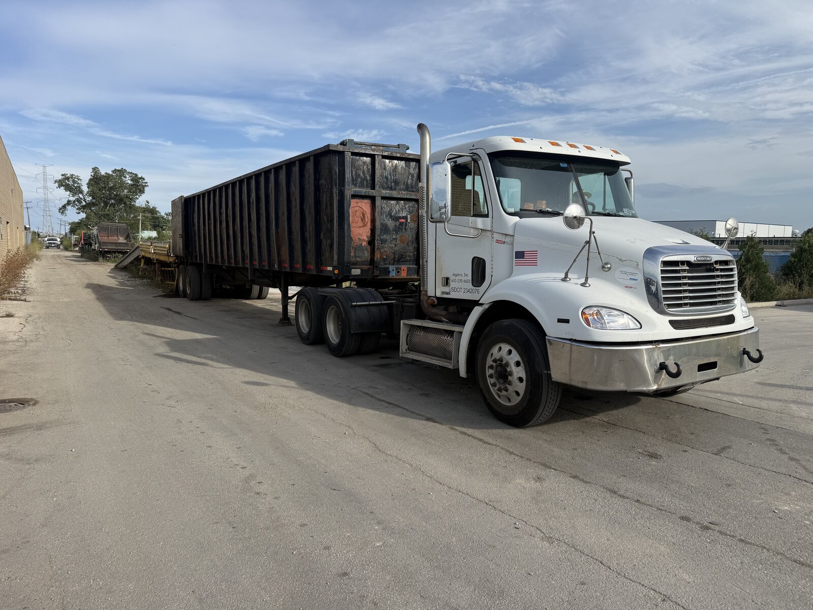 Our white Freightliner semi with a black scrap gondola trailer, backed up toward the ramp and platform in the yard