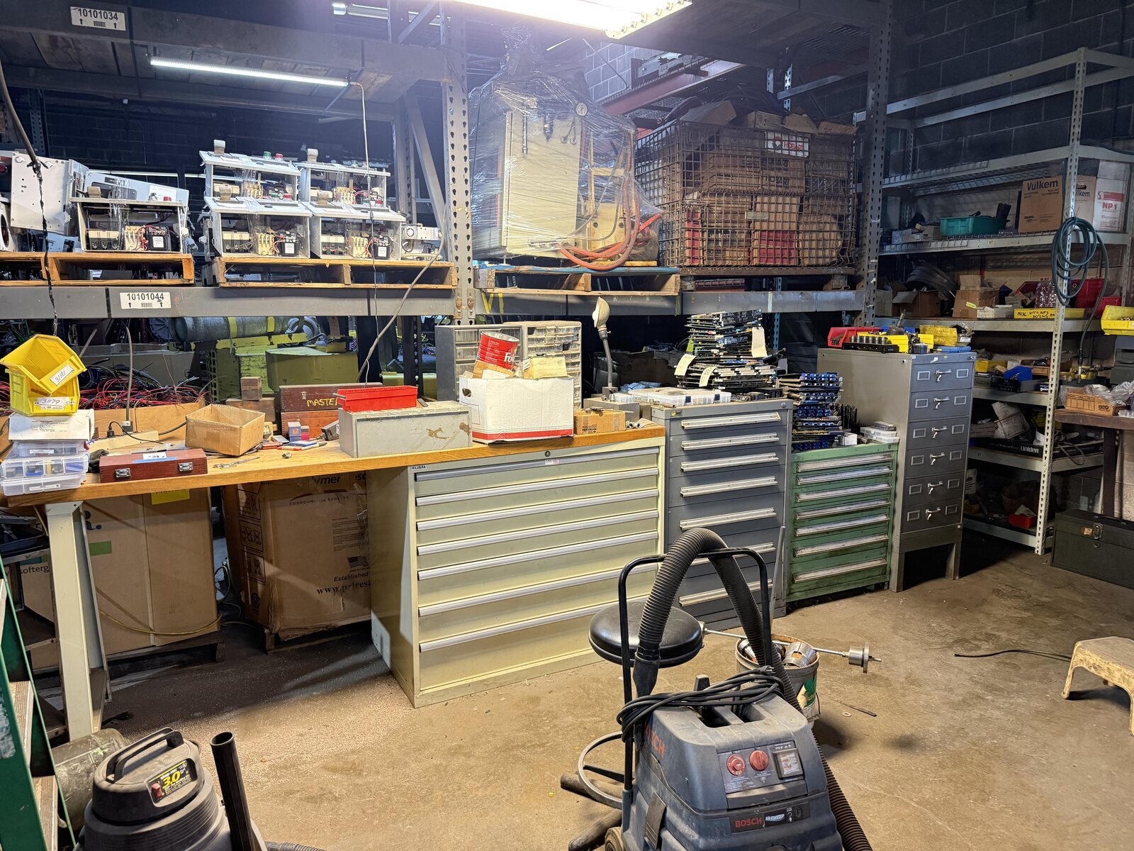 The long bench with tool cabinets and shelves of parts behind it