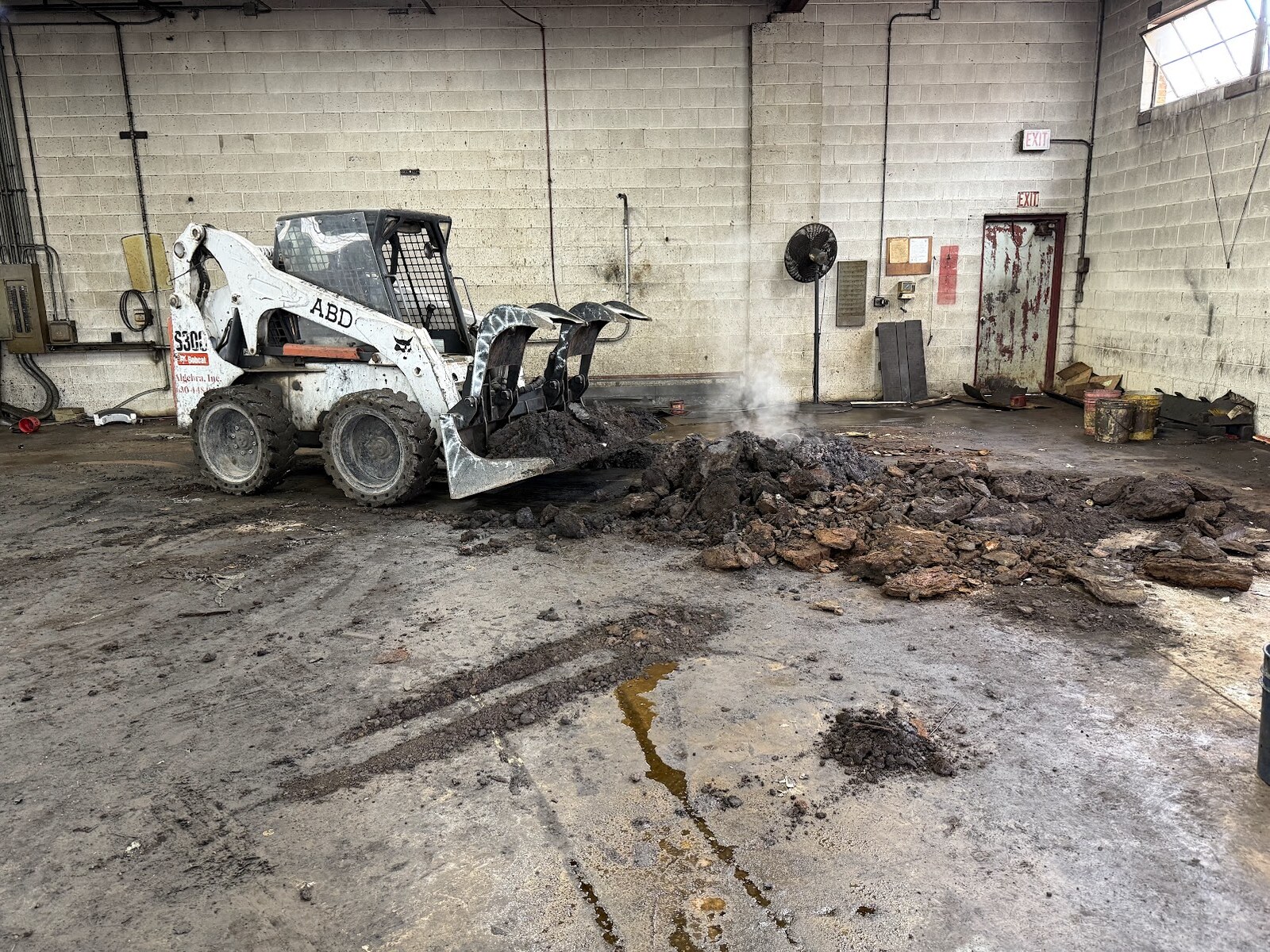 Our Bobcat S300 skid steer with a scrap grapple on it, clearing a pile of debris off a plant floor