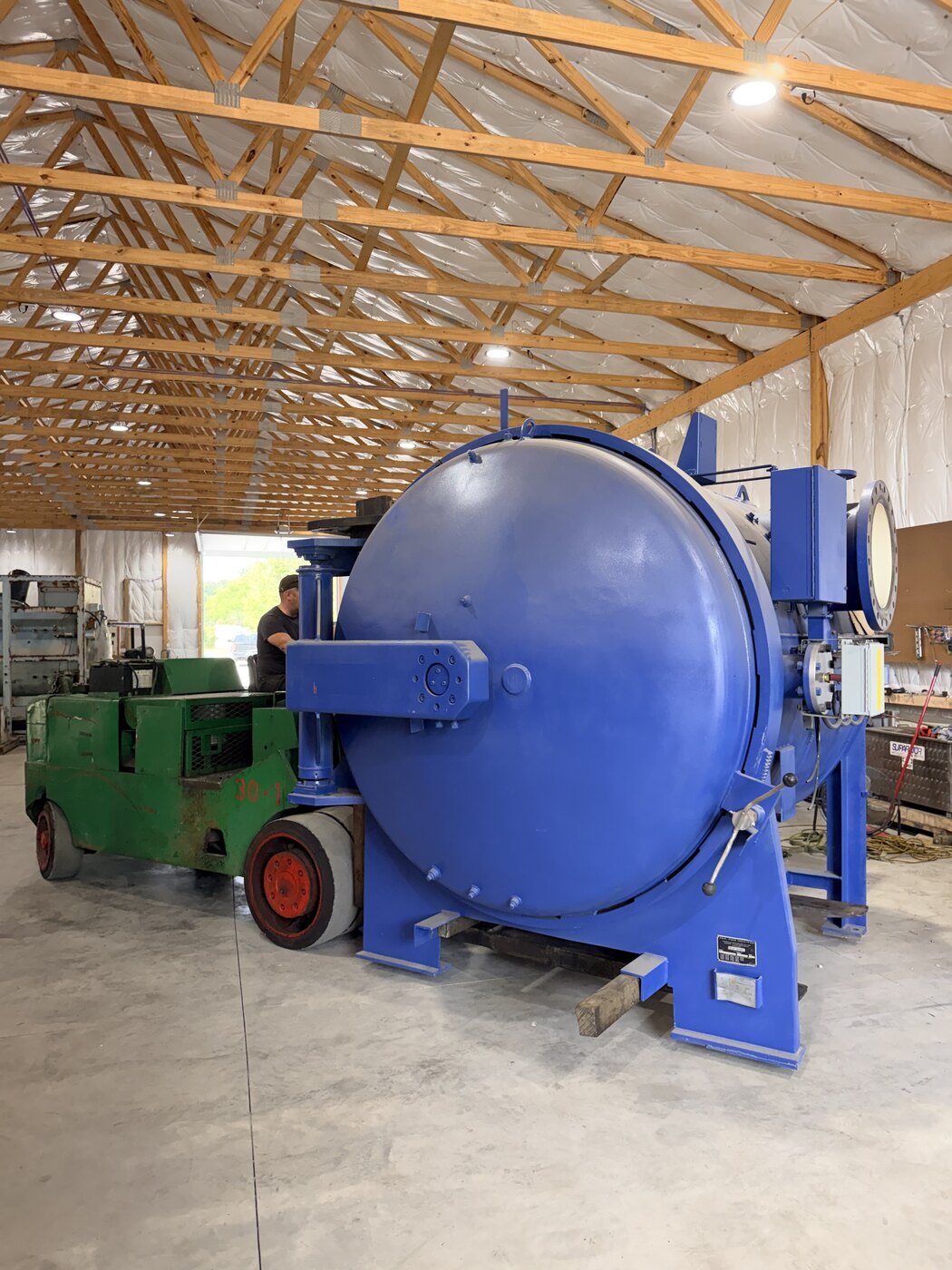 The blue vacuum furnace on the shop floor in Indiana, our green forklift behind it with the forks under the frame