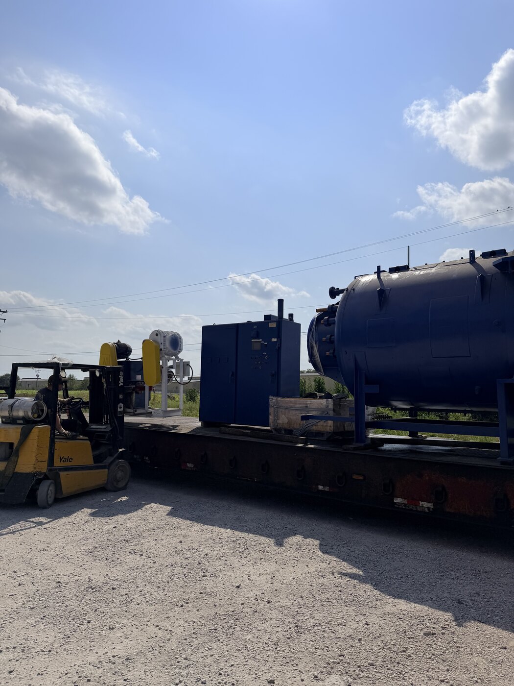 The lowboy with the furnace chamber and its blue control cabinet chained on, a yellow Yale forklift setting the next piece