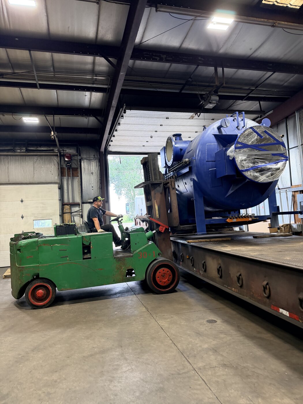 Our green forklift lifting the furnace chamber off the lowboy inside the receiving building, the overhead door open behind