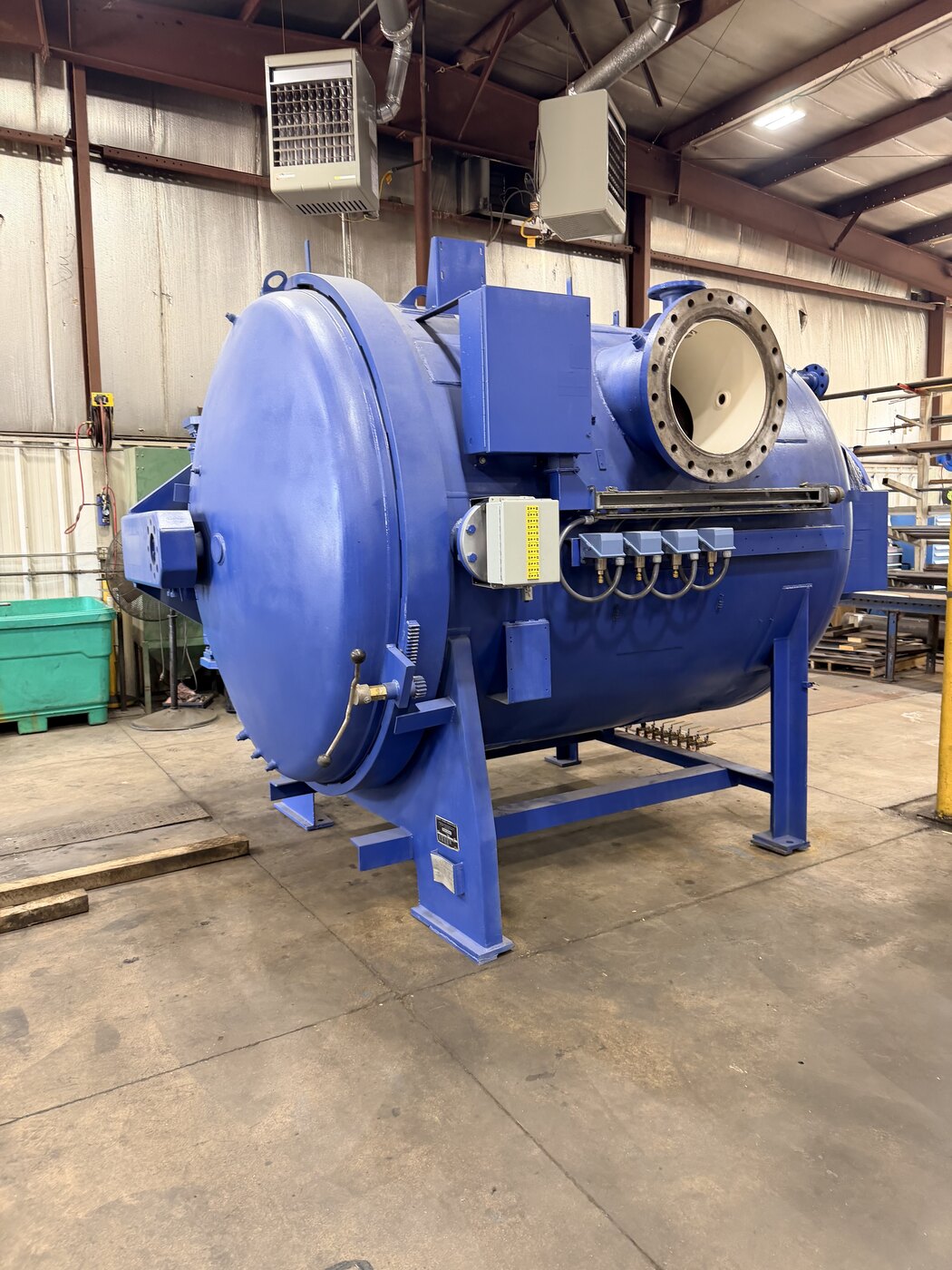 The vacuum furnace set down on the floor of the Wisconsin shop, control box and flanged port on the chamber, unloaded