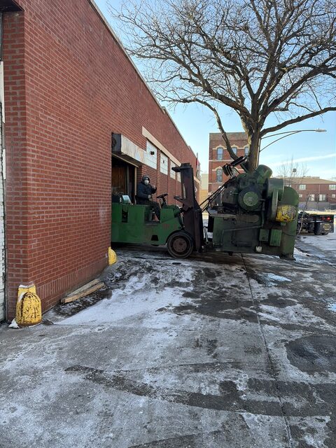 Our green forklift carrying a green machine out of a brick building in winter