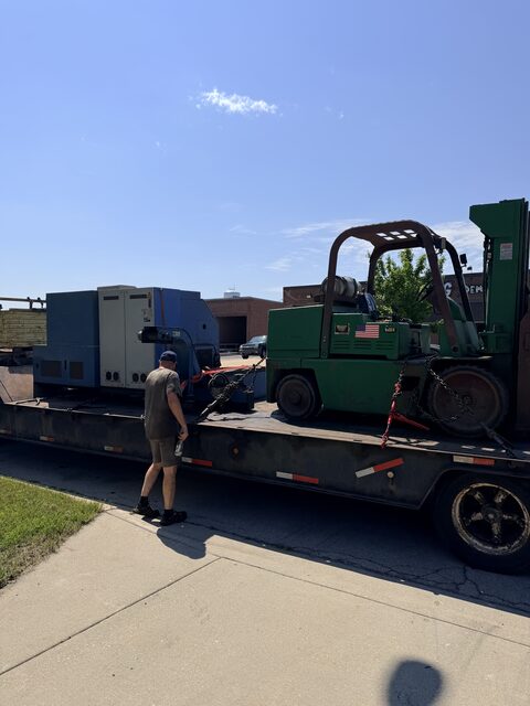 Our green forklift chained down on a trailer next to a blue machine