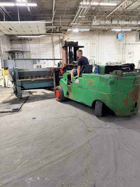 Our green forklift lifting a long blue shear in a shop