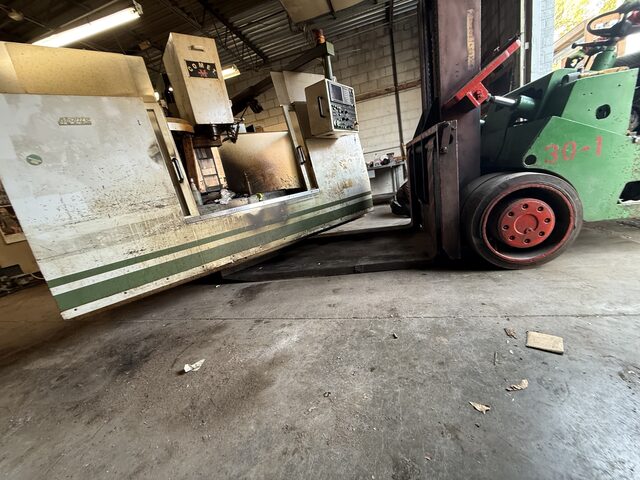 Our green forklift lifting the Mighty Comet vertical machining center inside the shop