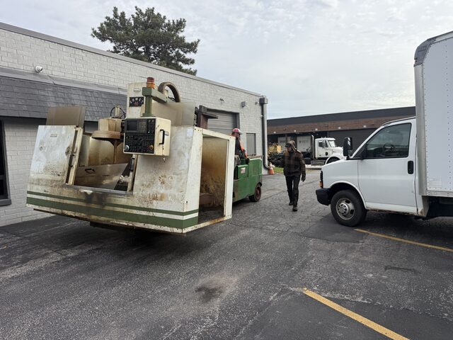 A machining center carried on the forks across a parking lot, past a box truck