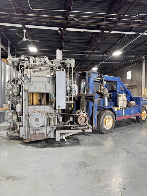 Our blue forklift carrying a tall gray press in a shop
