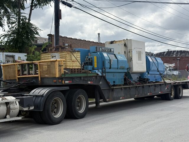 Blue CNC lathes, a white machine and a yellow cage on the lowboy trailer
