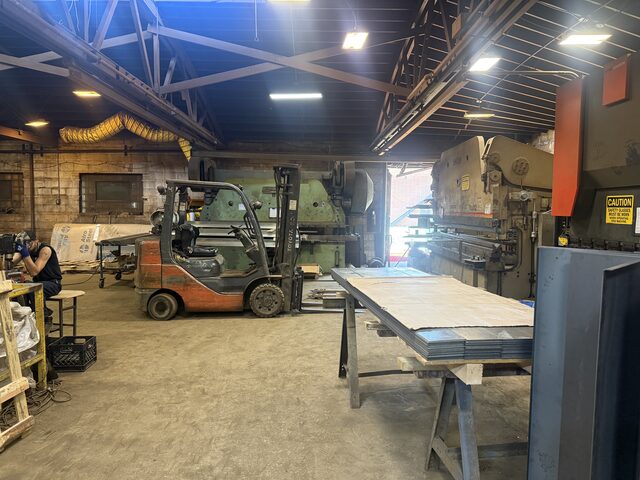 A shop with press brakes along the walls, a forklift and a long steel table