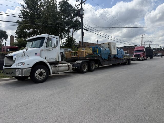 A truck and lowboy trailer loaded with machines, parked on a street