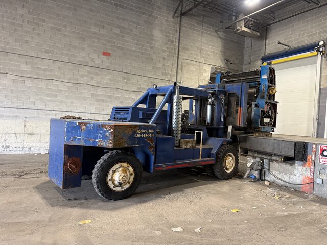 The blue forklift with the press unit at the edge of the dock