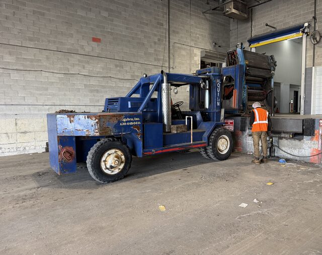Our blue forklift at the dock with a press unit on the forks