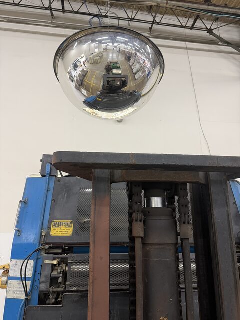 A ceiling dome mirror above the forklift mast, with the forklift reflected in it