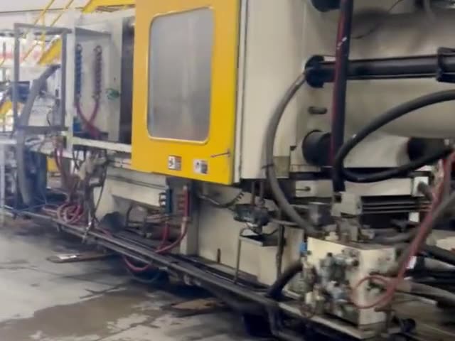 An injection molding machine with a yellow guard door, hydraulic hoses and valve blocks along its base
